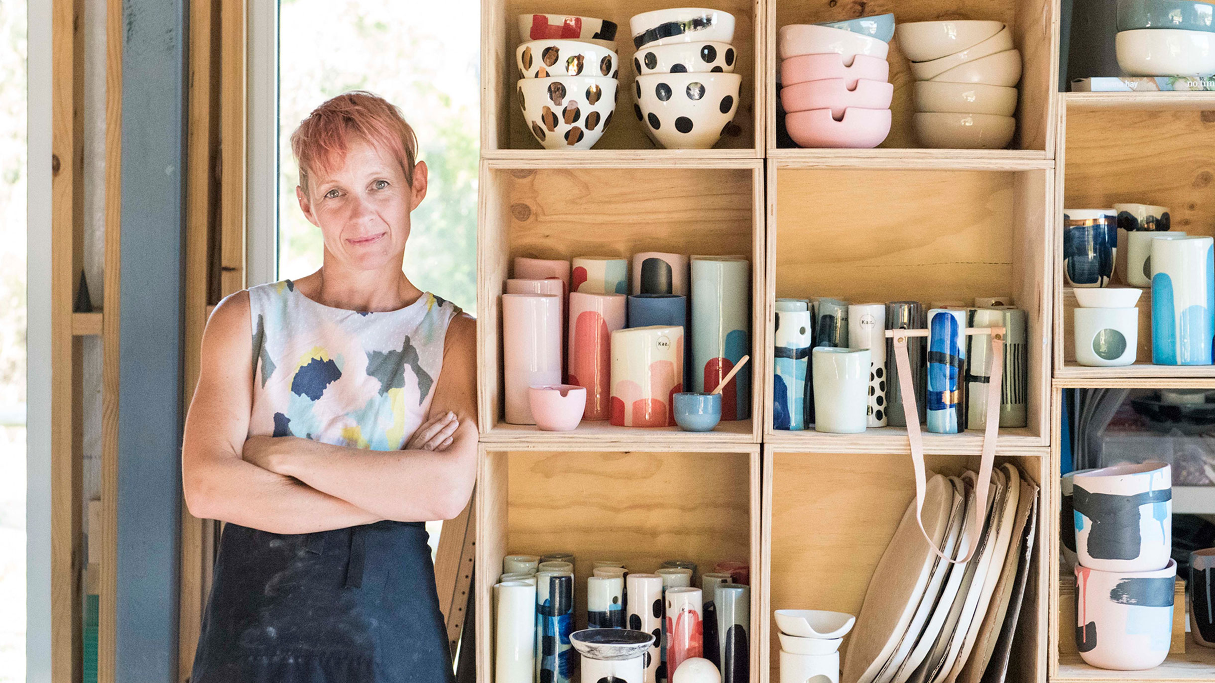 Karen Morton from Kaz Ceramics leans against shelves filled with pottery