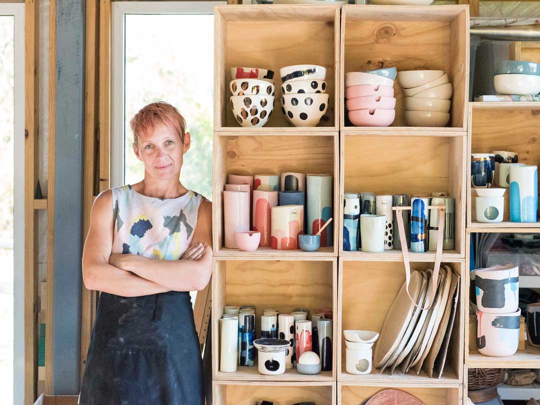 Karen Morton from Kaz Ceramics stands next to shelves filled with her pottery