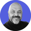 Smiling bald man with a beard wearing a black shirt, set against a solid blue circular background.